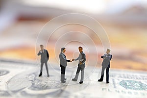 Miniature people: Businessman handshake with money on world map,  Investment, agreement, partnership and business concept