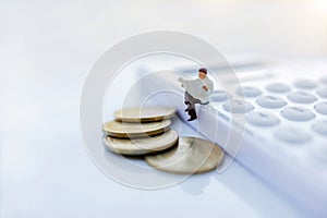 Miniature people: Businessman reading a book with coins and sitting on the calculator and calendar. Education or business concept