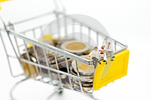 Miniature people : Businessman reading on shopping cart on stack of coin. Image use for retail business concept