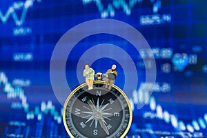 Miniature people: Businessman sitting on compass guide front of dashboard, display graphs, profit margins of background.