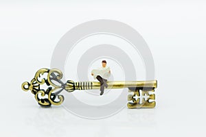 Miniature people: Businessman sitting on key and reading newspaper. Image use for key man, the key to success, business concept