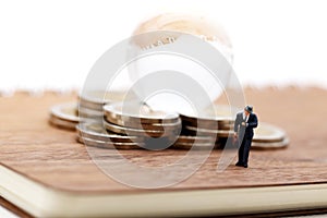Miniature people: Businessman standing on book with step of coin