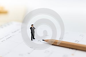 Miniature people : Businessman standing on the calendar to set the date for the meeting . Image use for business meetings concept