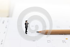 Miniature people : Businessman standing on the calendar to set the date for the meeting . Image use for business meetings concept