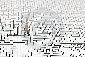 Miniature people: Businessman standing on center of maze. Concepts of finding a solution, problem solving and challenge.