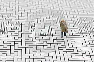 Miniature people: Businessman standing on center of maze. Concepts of finding a solution, problem solving and challenge.