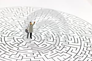 Miniature people: Businessman standing on center of maze. Concepts of finding a solution, problem solving and challenge.