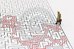 Miniature people: Businessman standing on center of maze. Concepts of finding a solution, problem solving and challenge.