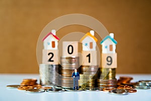 Miniature people, businessman standing with mini house, wooden block 2019 and pile of coins background using as financial, job