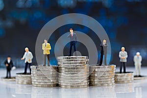 Miniature people : Businessman standing on stack of coins. Image use for difference in job position of business