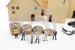 Miniature people: Businessmen shaking hands on coins stack with house and car.