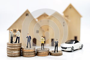 Miniature people: Businessmen shaking hands on coins stack with house and car.