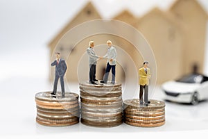 Miniature people:  Businessmen shaking hands on coins stack with house and car.  Concept of investment in housing.