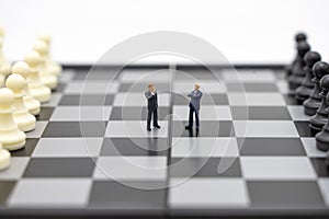 Miniature people businessmen standing on a chessboard with a chess piece on the back Negotiating in business. as background