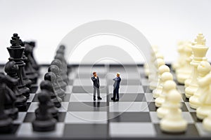 Miniature people businessmen standing on a chessboard with a chess piece on the back Negotiating in business. as background