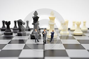 Miniature people businessmen standing on a chessboard with a chess piece on the back Negotiating in business. as background