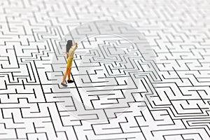 Miniature people: Businesswoman standing on center of maze. Concepts of finding a solution, problem solving and challenge.