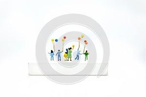 Miniature people, children holding colorful balloon on white box. White block can write anything for various occasions