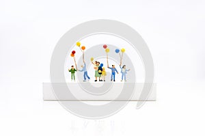 Miniature people, children holding colorful balloon on white box. White block can write anything for various occasions