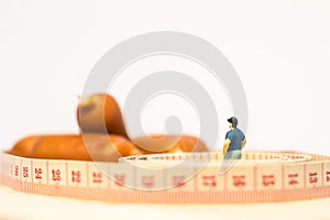 Miniature people : Close up fat man standing in waist tape measure and looking at sausages