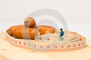 Miniature people : Close up fat man standing in waist tape measure and looking at sausages