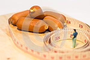 Miniature people : Close up fat man standing in waist tape measure and looking at sausages