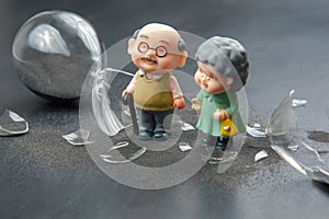 miniature people. couple of elderly people near a broken hourglass. life time crisis. the concept of the end of life for a person