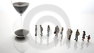 Miniature people. different people are walking next to the hourglass on a white background. lifespan of humanity