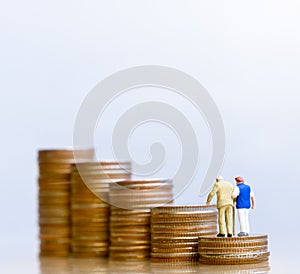 Miniature people: Elderly people sitting on coins stack.