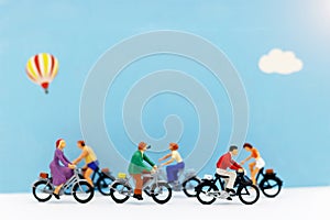 Miniature people enjoy riding a bicycle on blue background