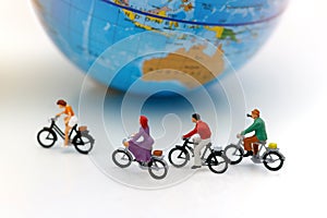 Miniature people enjoy riding a bicycle with globe