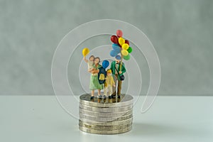 Miniature people, family holding balloon standing on stack of coins as financial business or happy retirement concept