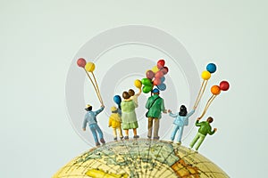 miniature people figure back view of happy family holding balloons standing on globe as looking into the universe or happy