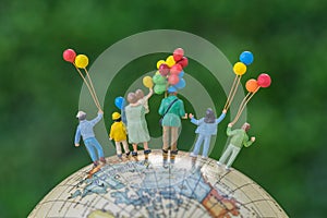 miniature people figure back view of happy family holding balloons standing on globe as world climate change environment or happy