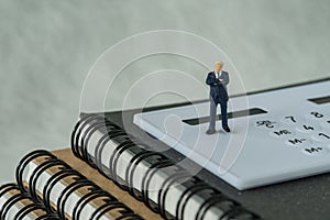 Miniature people figure businessman standing on white calculator