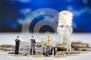 Miniature people, Group Businessmen standing on the coins, thinking solution for the business, light of lamp is idea.