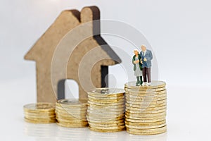 Miniature people: Happy senior couple standing on coins stack wi