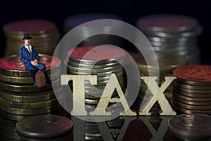 Miniature People. Man sitting on coin stacks with Text. IRPF Taxman Concept. Macro photo