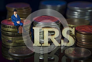 Miniature People. Man sitting on coin stacks with Text. IRS Taxman Concept. Macro photo