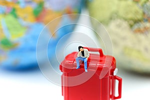Miniature people : man sitting on red suitcase with mini global