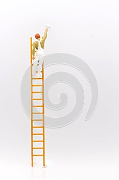 Miniature people, mini figure with ladder and white paint in front of a wall.