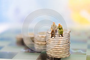 Miniature people, old couple figure standing on top of stack coins . Image use for background retirement planning,