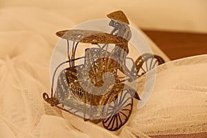 Miniature people pedaling a trishaw on a table and white cloth made of brass