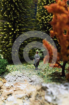 Miniature people: relaxed businessman standing in the forest. Working outdoor green nature concept. Macro photo, shallow DOF.