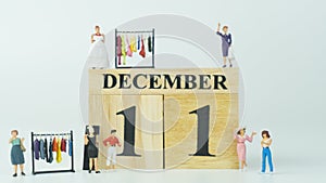 Miniature people Shopping at Women`s clothing store.Wooden letters write the word December and the numbers 11 on white background