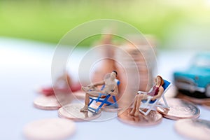 Miniature people sitting on beach sunbath seats and  coins stack.