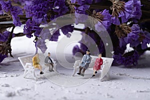 Miniature people sitting on a chair in a purple flower garden