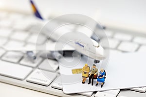 Miniature people sitting on credit card with keyboard and airplane
