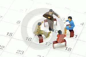 Miniature 4 people sitting on red staples placed on a white Calendar. meeting or Discussion using as background business concept