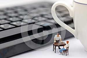 Miniature people sitting on table with keyboard and cup of coffee